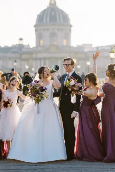 A joyful bride drinking champagne on a Paris bridge with a French wedding photographer capturing the moment.