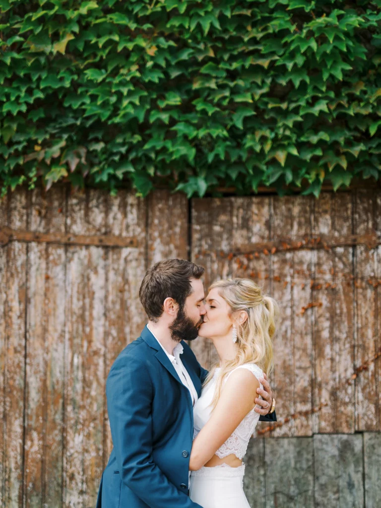 Couple s'embrassant devant une porte rustique couverte de lierre, par un photographe de mariage.