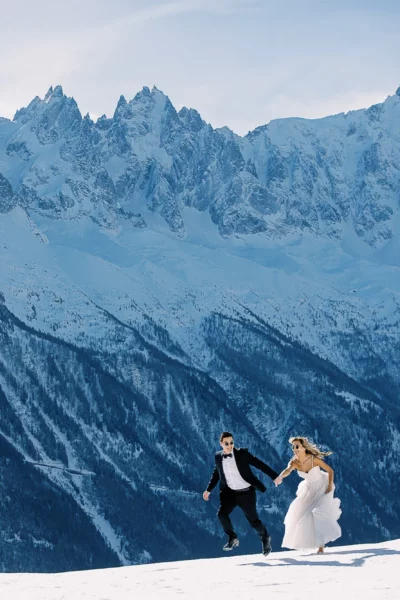 A joyful couple jumping in the snow, captured by a French wedding photographer in the Alps.