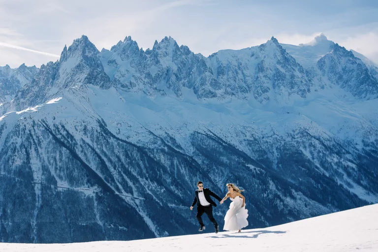 A joyful couple jumping in the snow, captured by a French wedding photographer in the Alps.