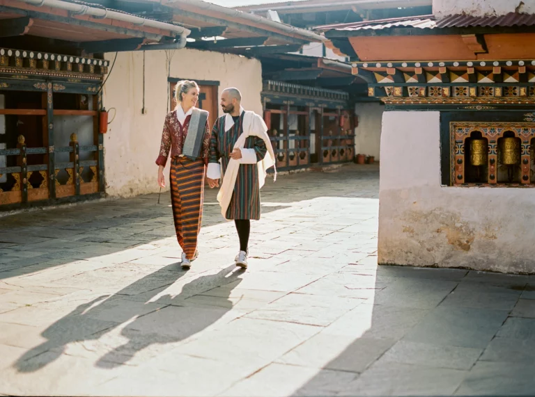 Couple en costume traditionnel bhoutanais marchant dans un monastère, par un photographe de mariage.