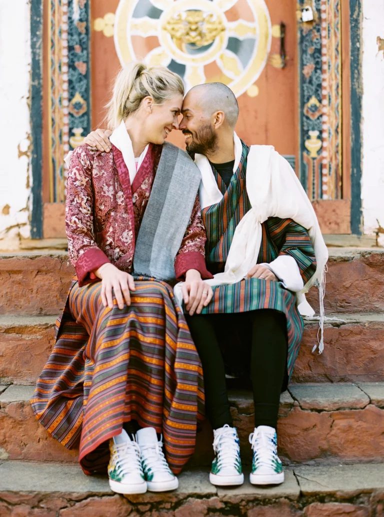 Couple en tenue traditionnelle bhoutanaise sur les marches d'un temple par un photographe de mariage.