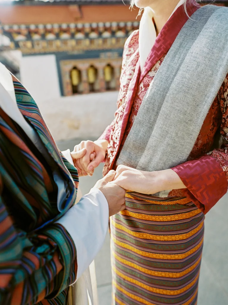 Gros plan d'un couple se tenant la main en tenue traditionnelle bhoutanaise par un photographe de mariage.
