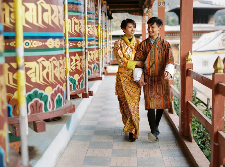 Couple en tenue traditionnelle bhoutanaise marchant près de moulins à prière, photographe de couple.