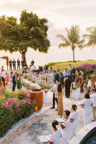 Guests mingling at a luxury seaside ceremony captured by a French wedding photographer during golden hour in Bali, Indonesia.
