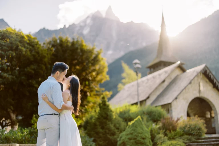 Couple s'embrassant devant une chapelle de montagne par un photographe de mariage.
