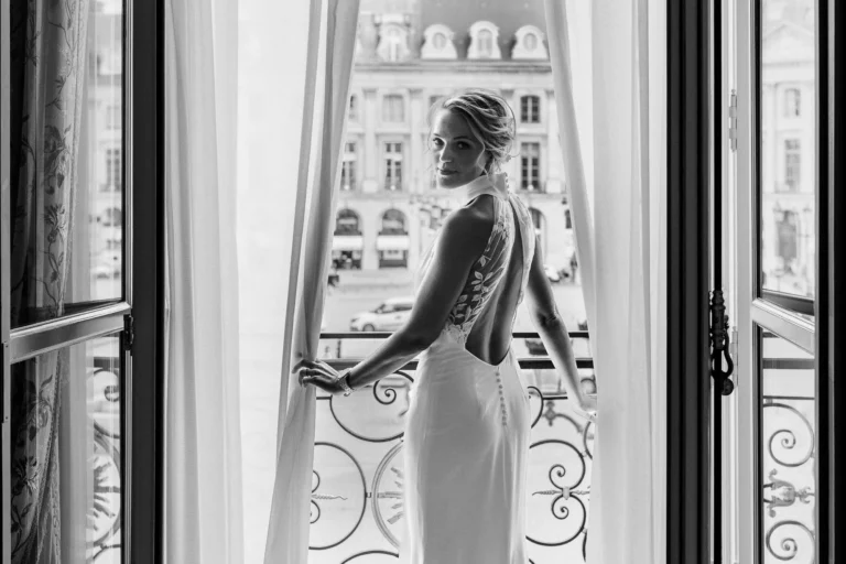 Elegant bride at a balcony window by a French wedding photographer wedding photographer in Paris.