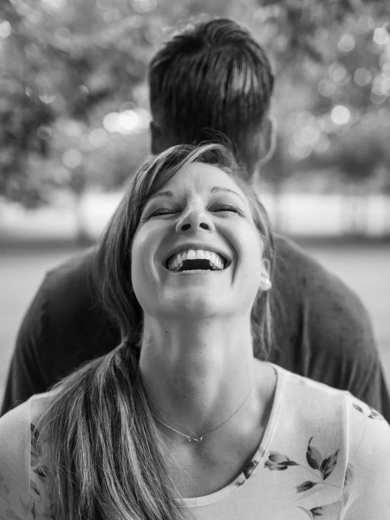 Une femme riant aux éclats lors d'une séance avec un photographe de couple en extérieur.