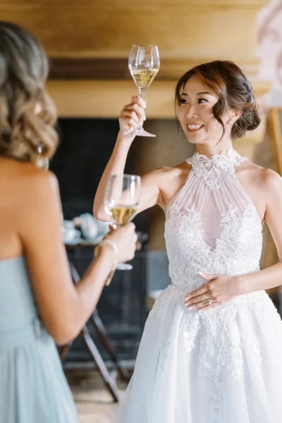 Bride in lace dress toasting bridesmaids during preparations by a French wedding photographer.