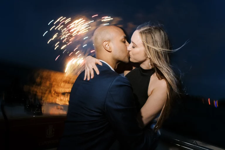 Un couple s'embrassant sur un bateau avec feu d'artifice, par un photographe de mariage.