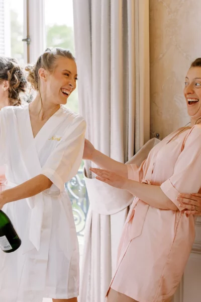Bride and bridesmaids opening champagne, captured by a French wedding photographer during luxury bridal preparations.