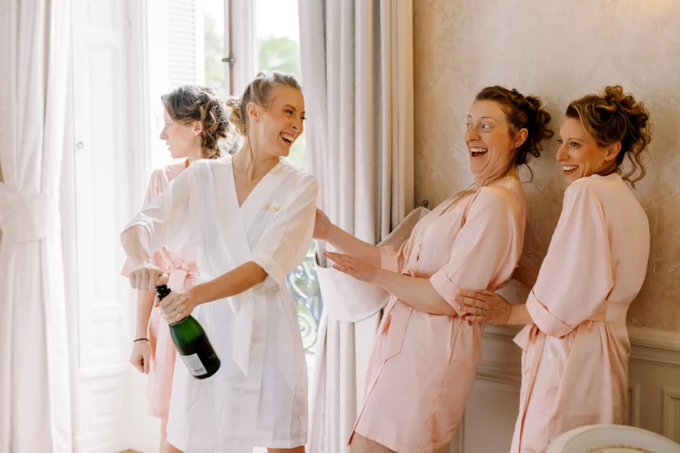 Bride and bridesmaids opening champagne, captured by a French wedding photographer during luxury bridal preparations.