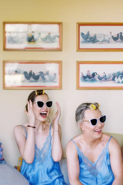 Joyful bridesmaids in blue silk robes with sunglasses captured by a French wedding photographer.