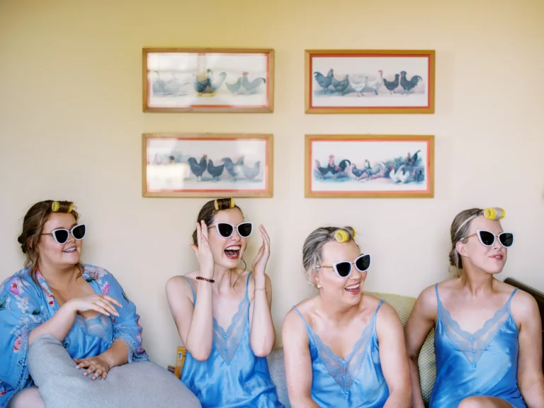 Joyful bridesmaids in blue silk robes with sunglasses captured by a French wedding photographer.