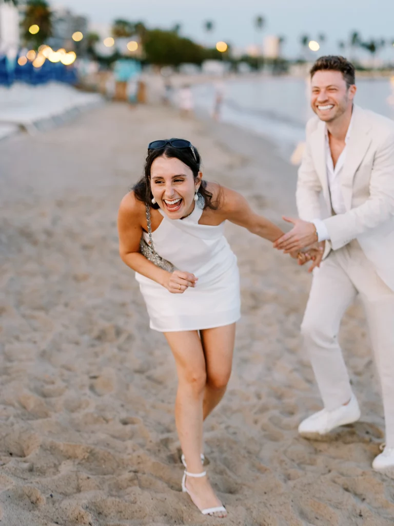 Un couple riant aux éclats sur la plage capturé par un photographe de couple.