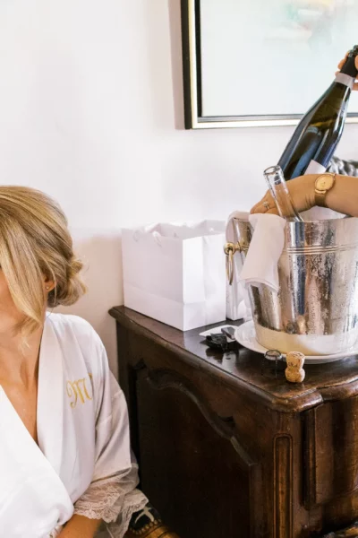 Bride in silk robe during champagne preparation captured by a French wedding photographer.