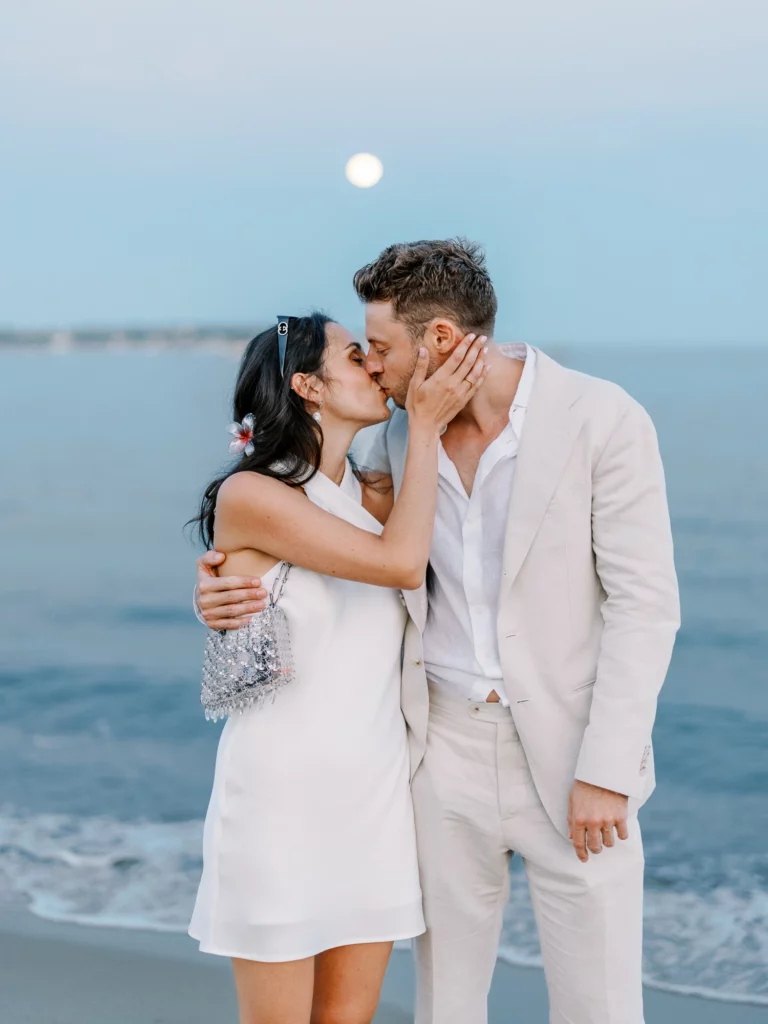 Un couple s'embrasse sur la plage sous la pleine lune, capturé par un photographe de couple.