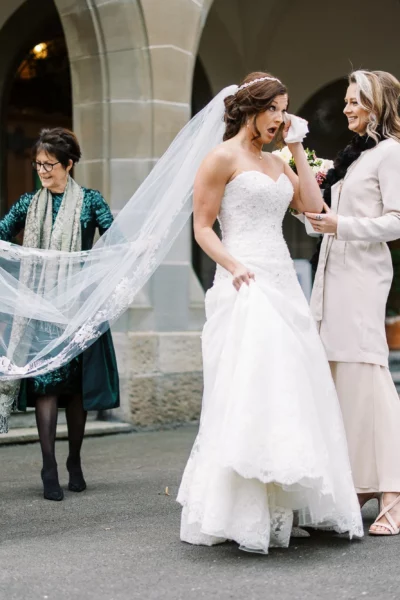 Emotional bride wiping away tears beside a vintage Rolls Royce, captured by a French wedding photographer.