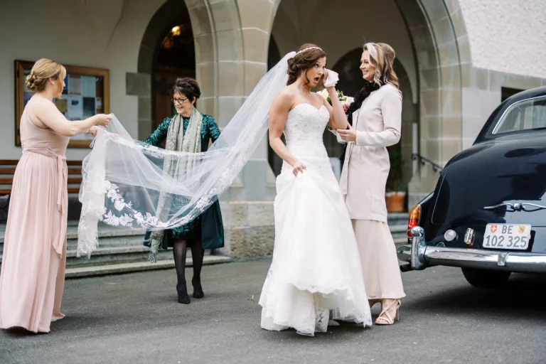 Emotional bride wiping away tears beside a vintage Rolls Royce, captured by a French wedding photographer.