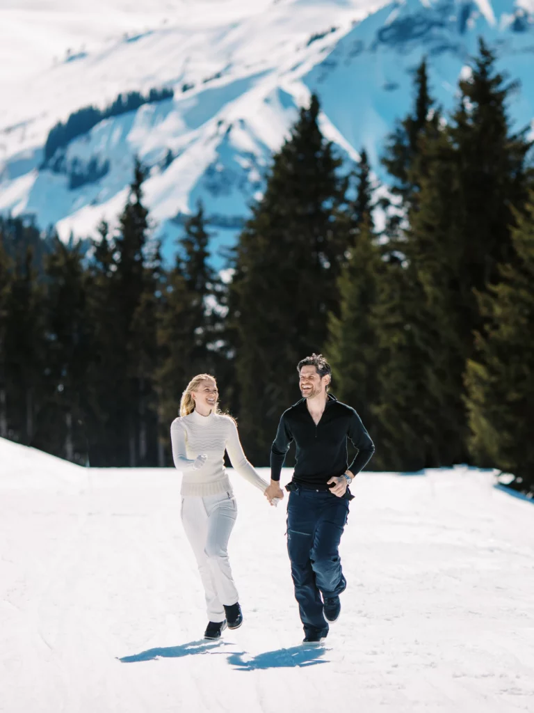 Couple joyeux courant dans la neige alpine lors d'une séance photo de couple wedding photographer.