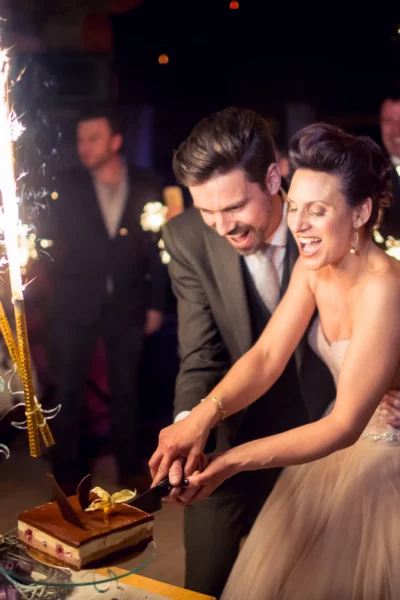 Joyful bride and groom cutting cake with sparklers by a French wedding photographer.