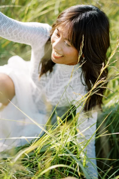 A bride in a lace gown smiling in tall grass, captured by a French wedding photographer.