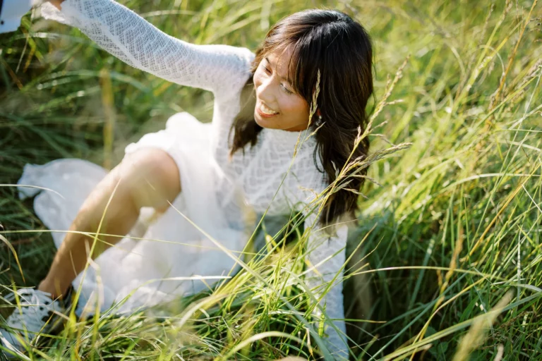 A bride in a lace gown smiling in tall grass, captured by a French wedding photographer.
