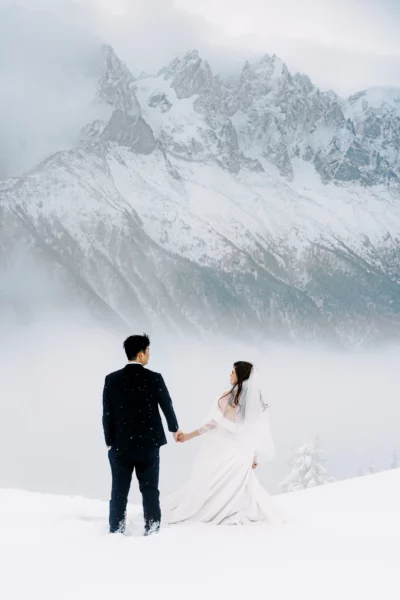 Couple overlooking snow-capped peaks with french wedding photographer capturing their winter elopement.