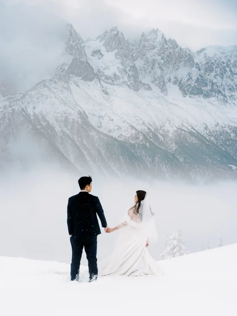 Couple overlooking snow-capped peaks with french wedding photographer wedding photographer capturing their winter elopement.