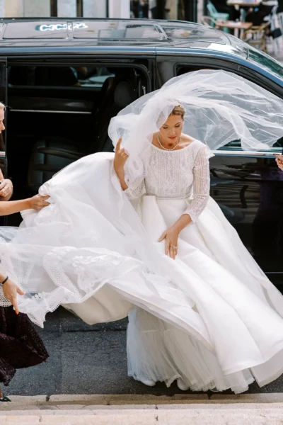 Bride exiting a black van assisted by bridesmaids, captured by a French wedding photographer.