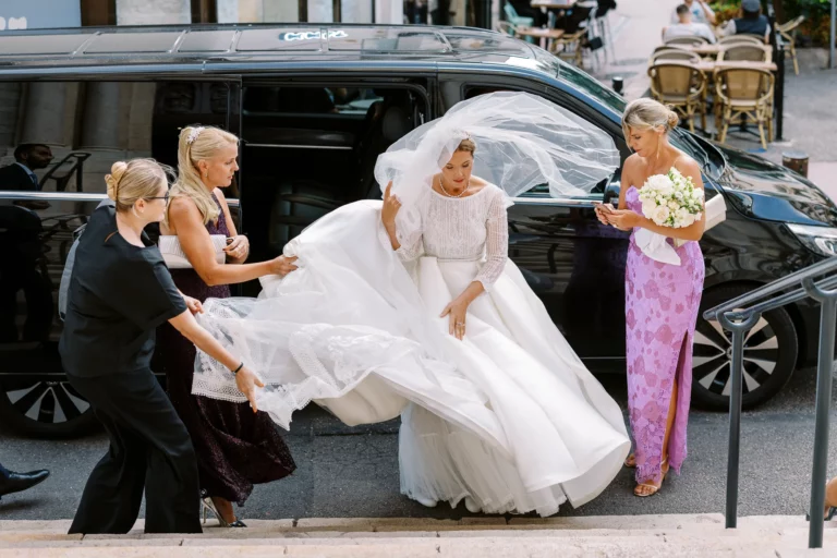 Bride exiting a black van assisted by bridesmaids, captured by a French wedding photographer.