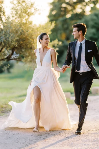 Joyful bride and groom walking through Provence olive groves captured by a French wedding photographer.