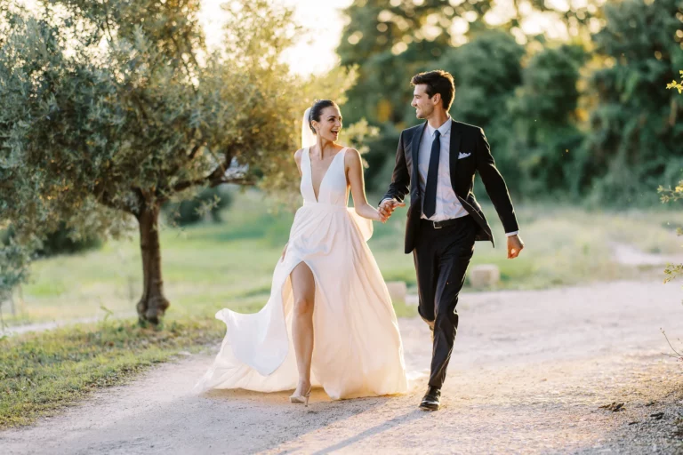 Joyful bride and groom walking through Provence olive groves captured by a French wedding photographer.