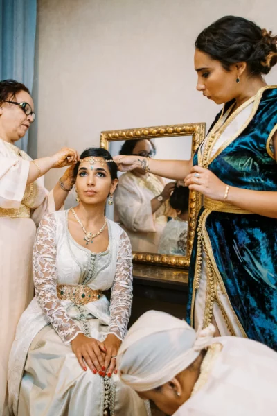 Moroccan bride in white lace kaftan assisted by family, french wedding photographer.