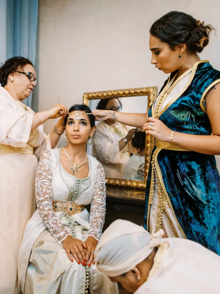 Moroccan bride in white lace kaftan assisted by family, french wedding photographer wedding photographer.