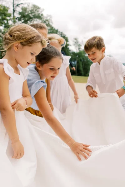Children gathering around a bridal veil captured by a French wedding photographer outdoors.