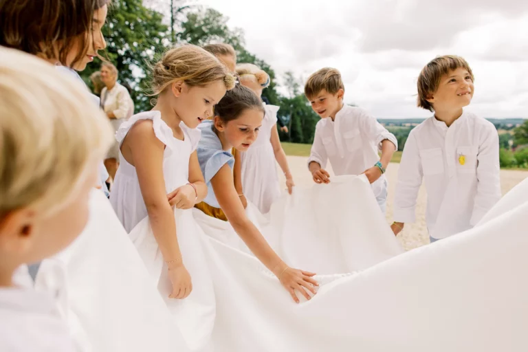 Children gathering around a bridal veil captured by a French wedding photographer outdoors.
