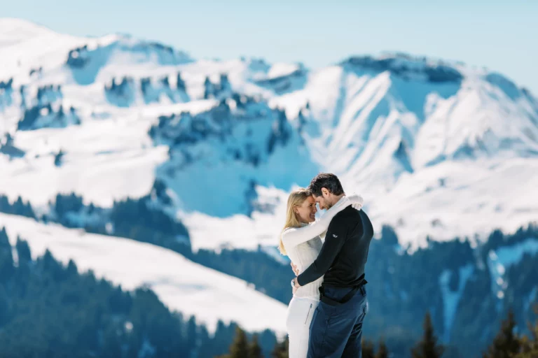 Un couple joyeux s'enlaçant dans les montagnes enneigées par un photographe spécialisé en photo de couple.
