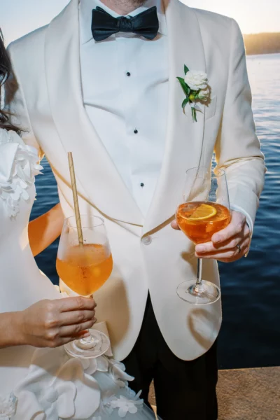 Bride and groom holding cocktails by the water, captured by a french wedding photographer.