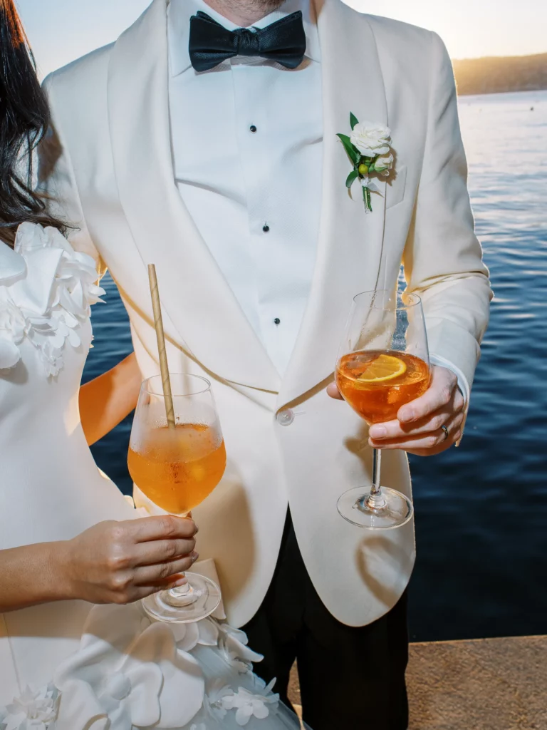 Bride and groom holding cocktails by the water, captured by a french wedding photographer.