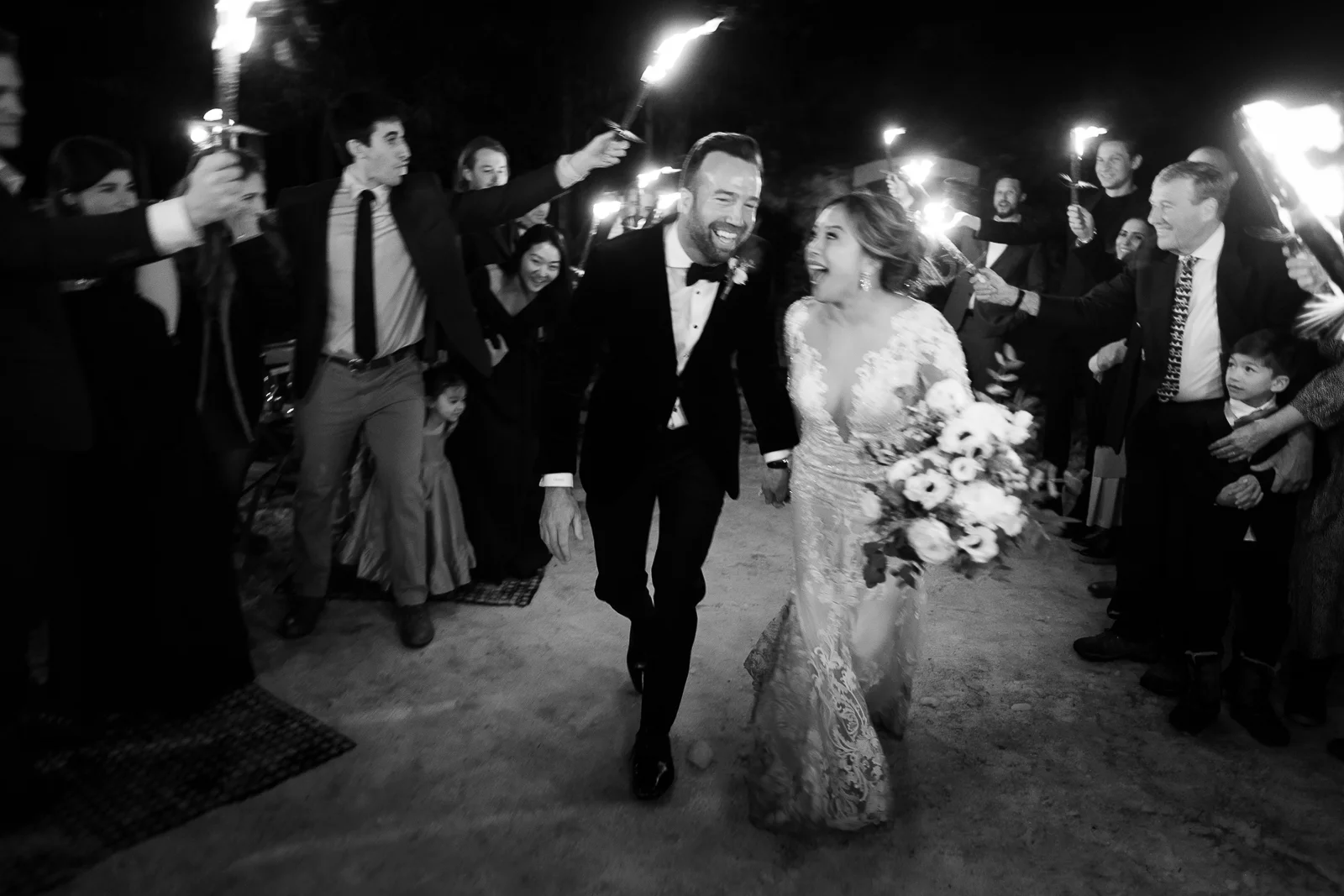 Couple joyeux courant lors d'une haie d'honneur aux flambeaux capturé par un photographe mariage France.