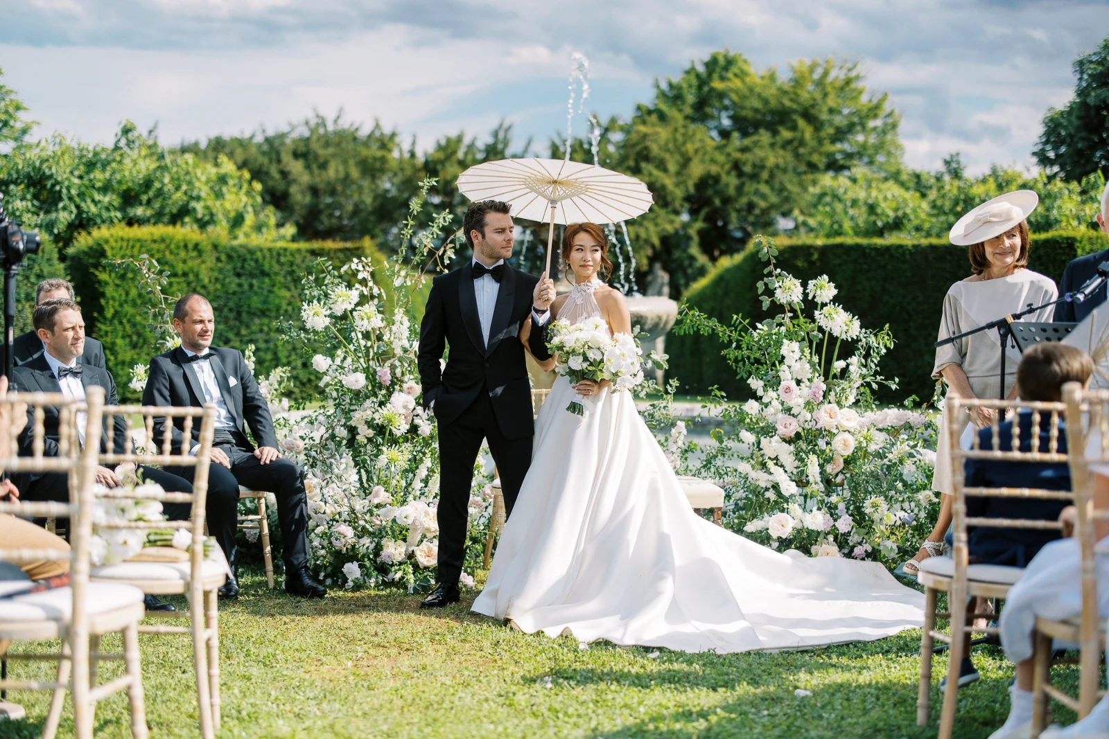 Bride and groom at a sun-drenched French Riviera wedding ceremony framed by lush white floral pillars.