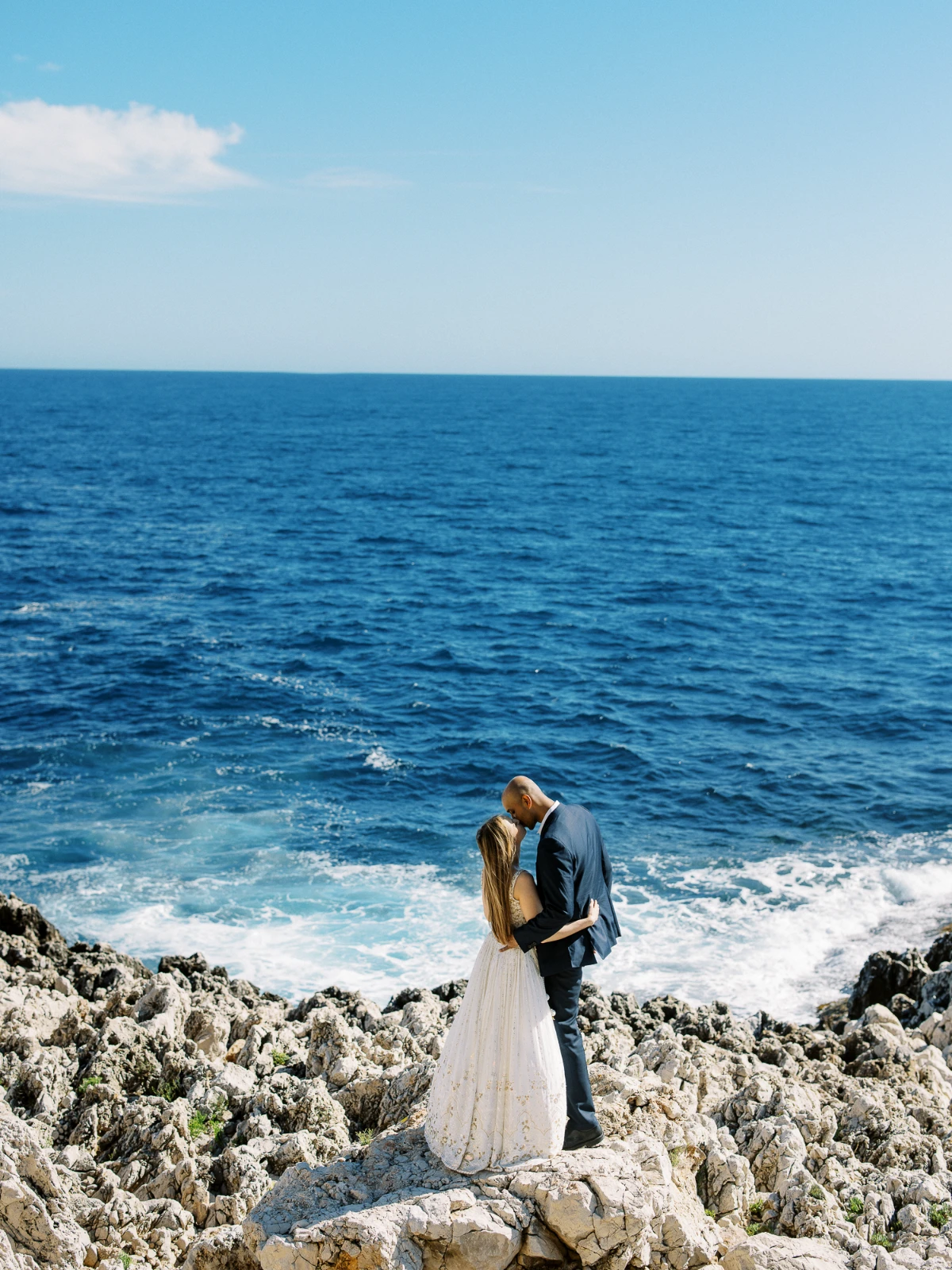 A Cannes wedding photographer captures a couple's kiss on the rocky French Riviera coastline.