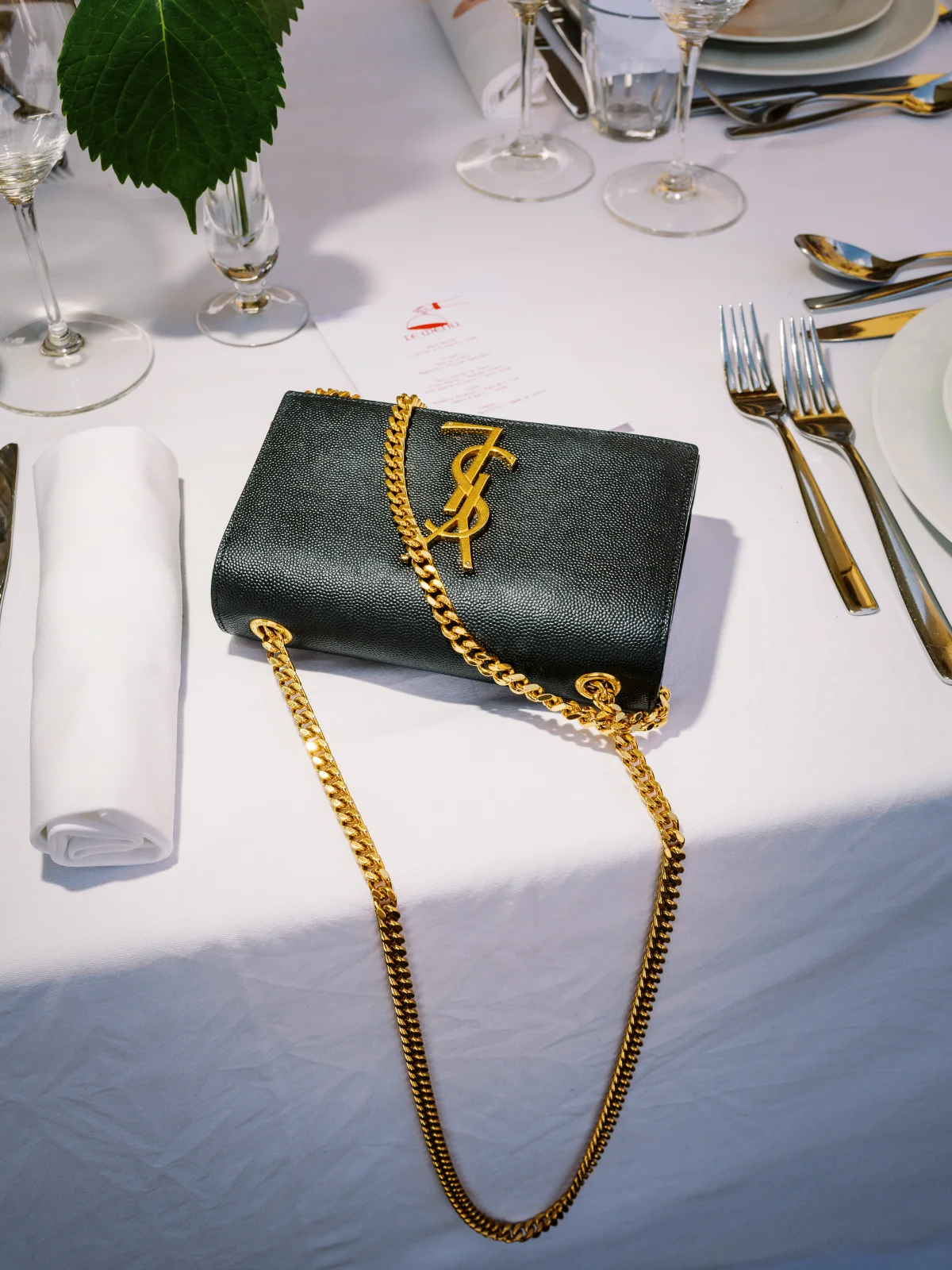 Sac à main de luxe noir à chaîne dorée posé sur une table de banquet pour se marier en Corse avec style.
