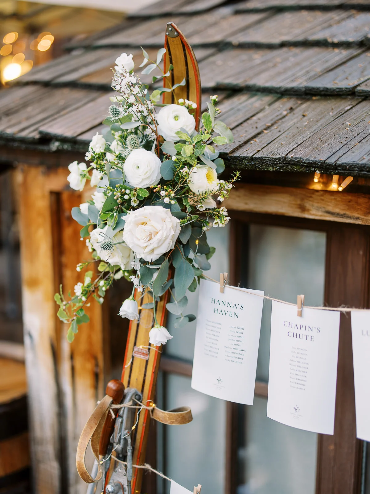 Vintage ski decorated with white roses and hanging seating charts for a St Moritz wedding reception.